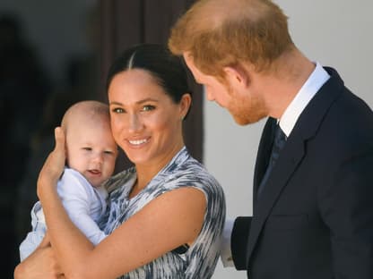 Meghan lächelt in die Kamera und hält Archie im Arm.