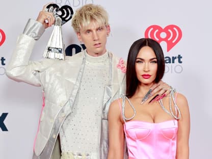 Machine Gun Kelly hält einen Award auf der Schulter, Megan Fox steht im rosanen Kleid neben ihm