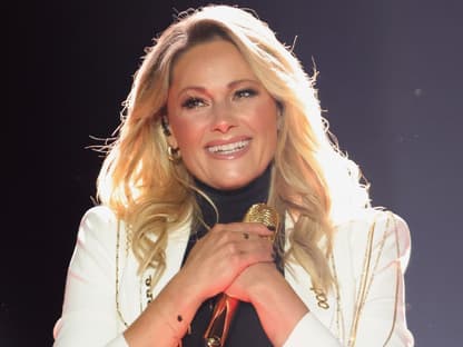 Helene Fischer strahlt und hat beide Hände um ihr Mikro was sie an ihr Herz hält.