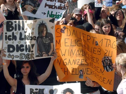 Fans warten vor einem Konzert und halten Plakate hoch