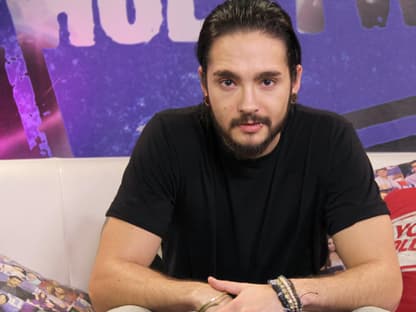 Tom Kaulitz sitzt auf Sofa und guckt in die Kamera