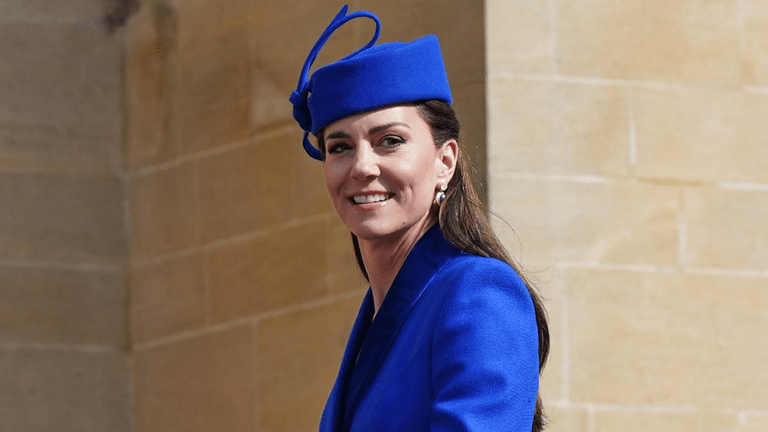 Prinzessin Kate im blauen Mantelkostüm lächelt in die Kamera.